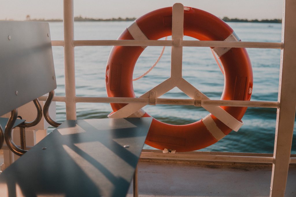 Photo of a bench on a boat in the water with an orange round life saver on the outside.