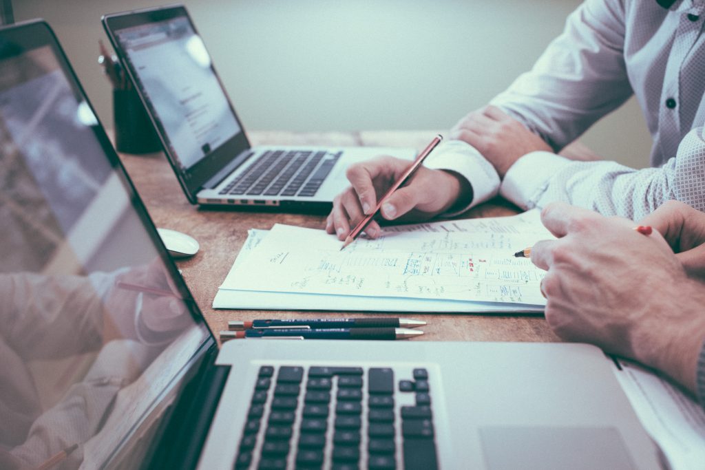 Photo of two business men sitting at a desk with laptops and reviewing papers.