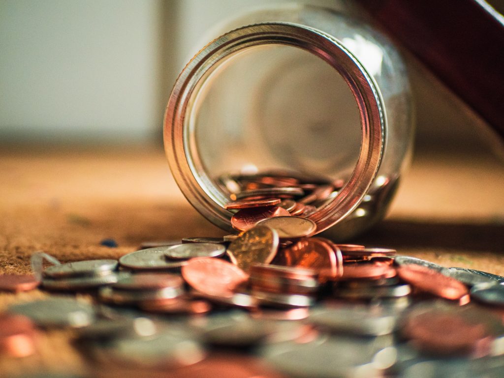 Close up photo of coins falling out of a tipped over glass jar.