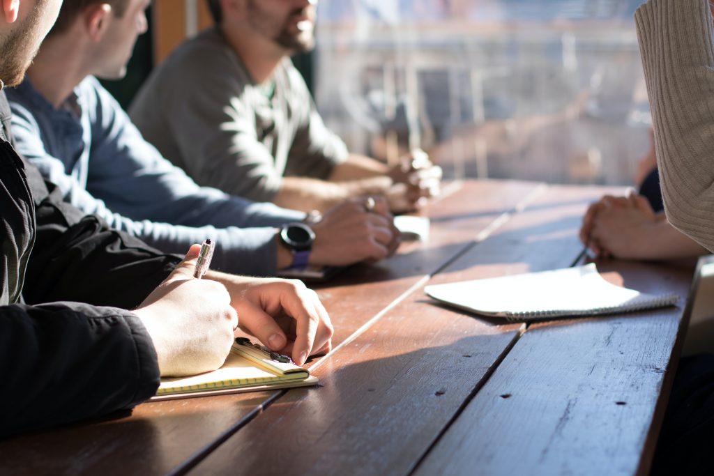 Photo of a group of people with notebooks having a discussion while sitting at a table.