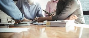 Close up shot of four people having a team meeting at table with many papers on it.