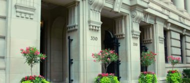 Photo of a large building with intricate architecture and decorative plants sitting in between entryways.