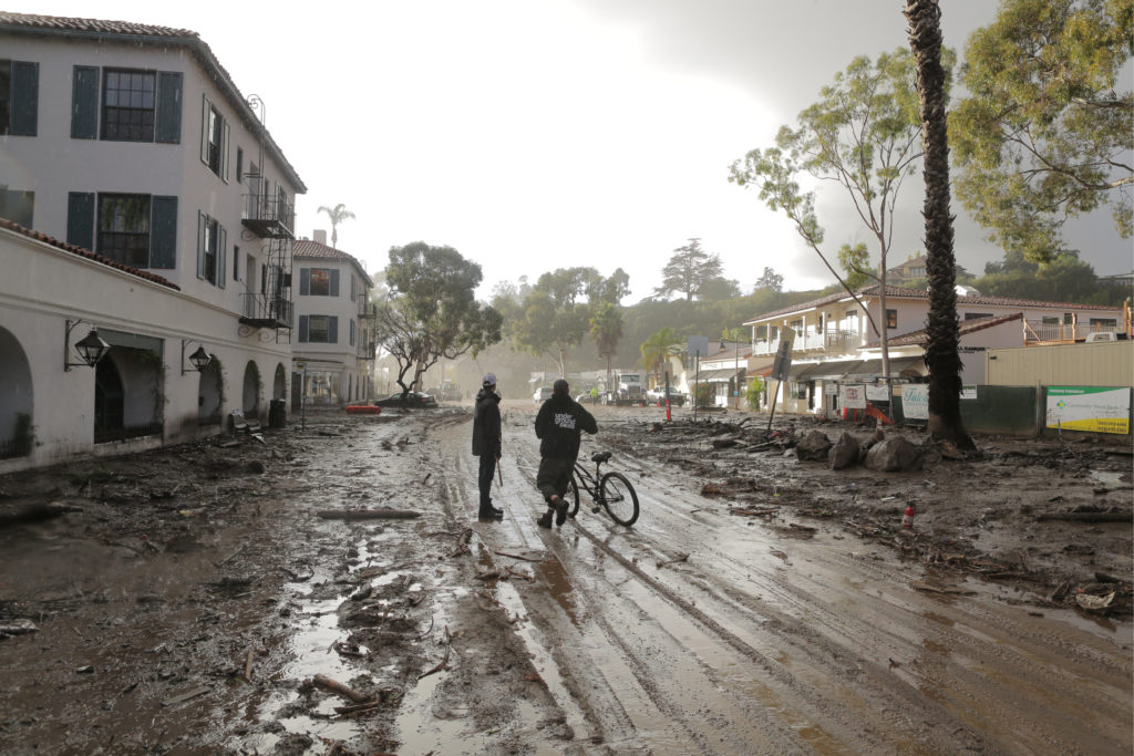 Two people standing in street covered with mud from flooding.