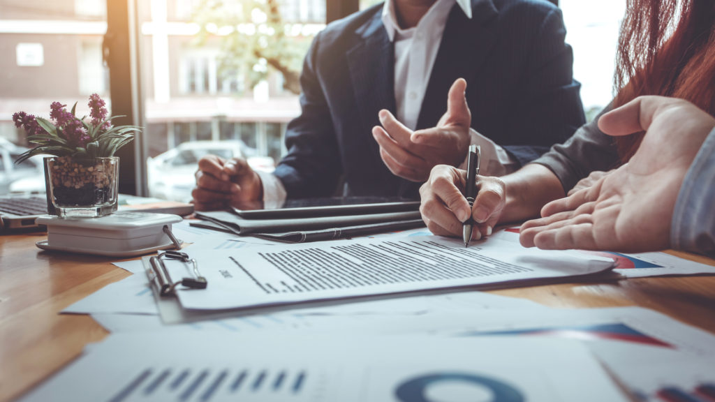 Three businesspeople working together on documents at conference table.